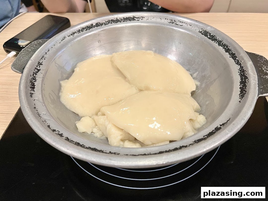 A metal pot filled with creamy, collagen-rich chicken stock on an induction cooker.