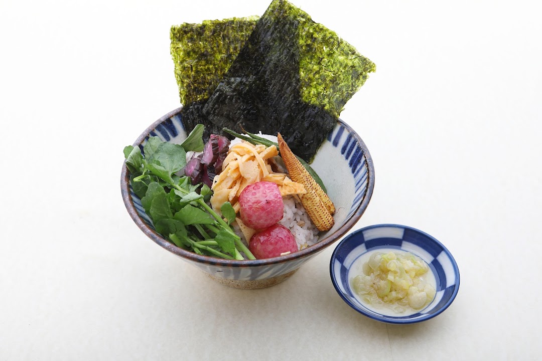 A vibrant Japanese rice bowl featuring fresh vegetables, radishes, baby corn, and nori.