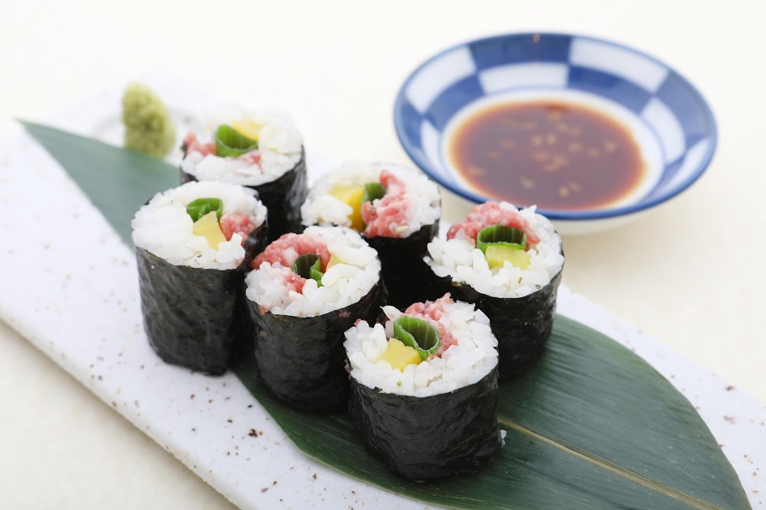 Close-up of six Japanese sushi rolls with rice, nori, and various fillings, served with wasabi and soy sauce.