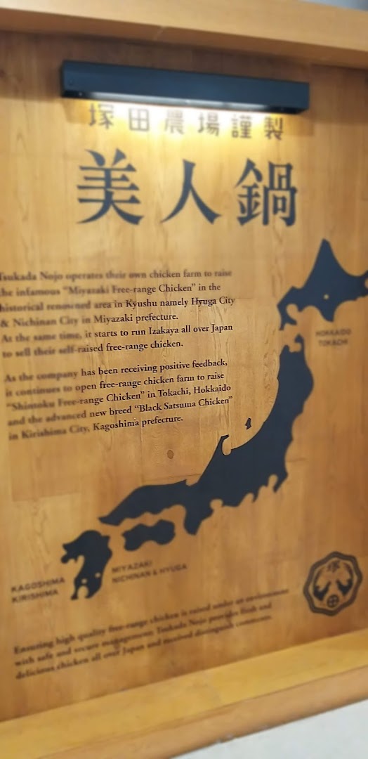 A wooden sign detailing Tsukada Nojo's commitment to sourcing premium free-range chicken from various Japanese prefectures.