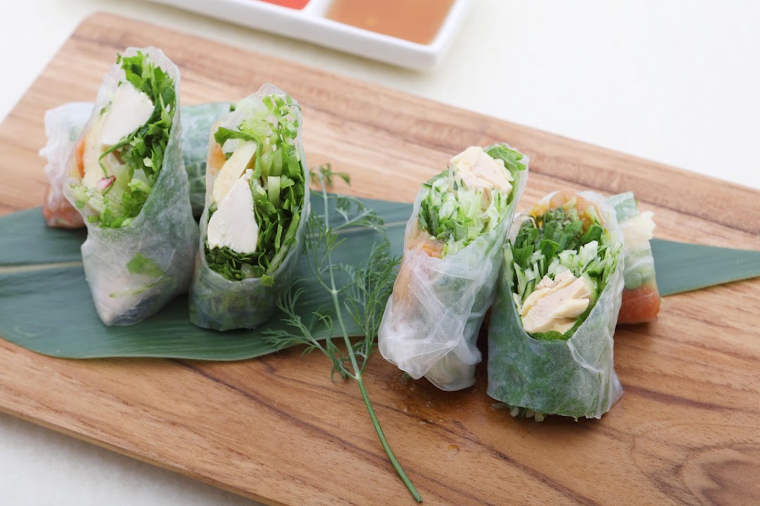 Fresh spring rolls filled with chicken and greens, served on a wooden board with dipping sauces.