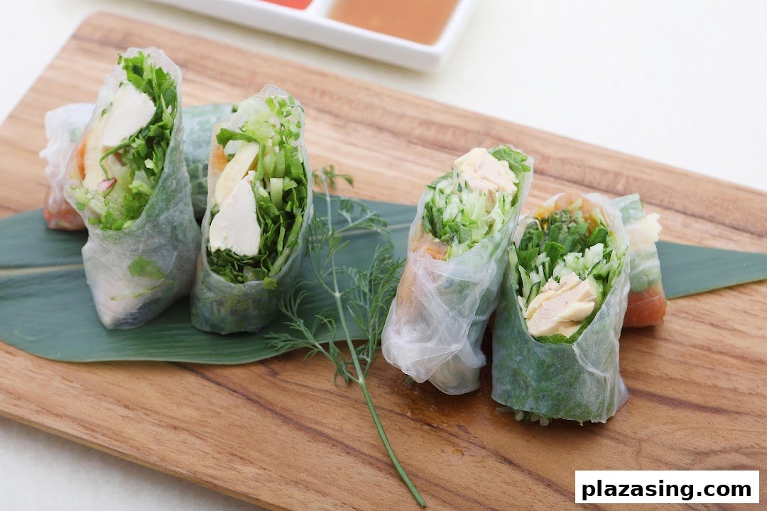 Fresh spring rolls filled with chicken and greens, served on a wooden board with dipping sauces.