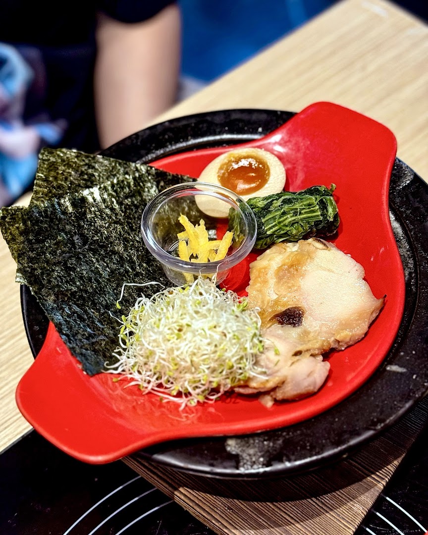 A vibrant red plate showcasing fresh hotpot ingredients including nori, sprouts, egg, and chicken.