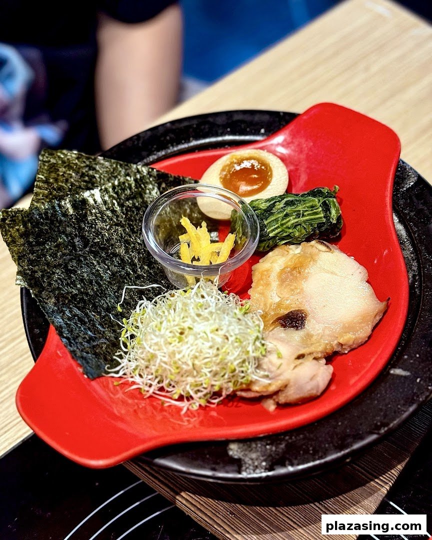 A vibrant red plate showcasing fresh hotpot ingredients including nori, sprouts, egg, and chicken.