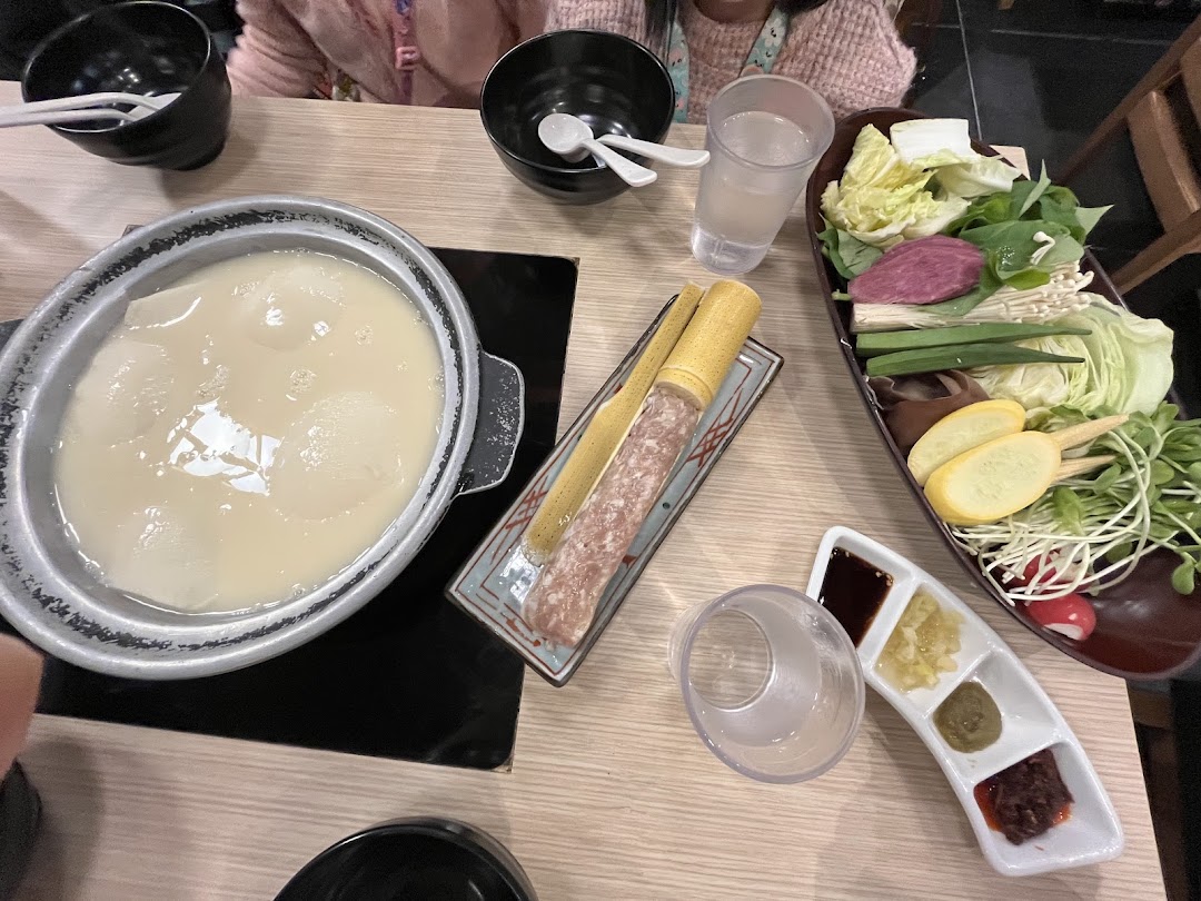 A hotpot meal with collagen broth, fresh vegetables, and meat paste on a dining table.