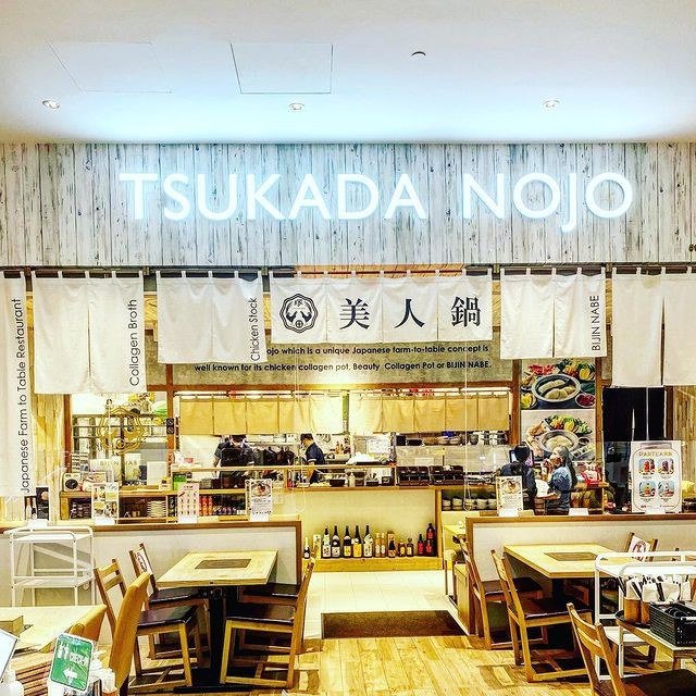 The illuminated entrance of Tsukada Nojo, a Japanese farm-to-table restaurant, showcasing its inviting dining area.