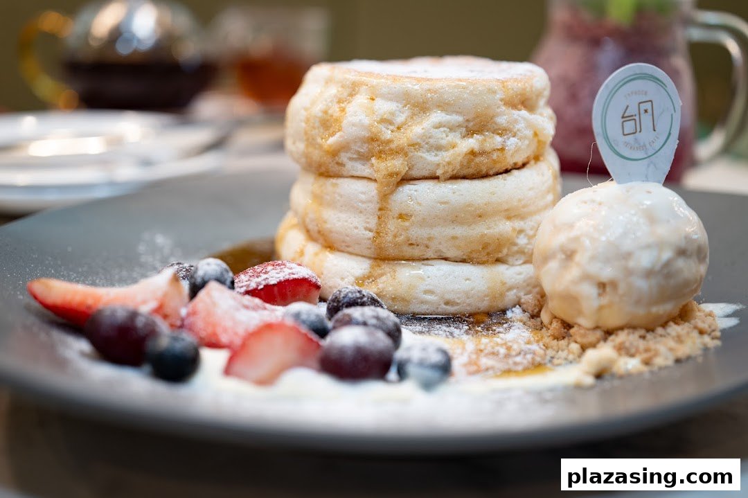 Fluffy soufflé pancakes with berries, ice cream, and syrup on a dark plate.