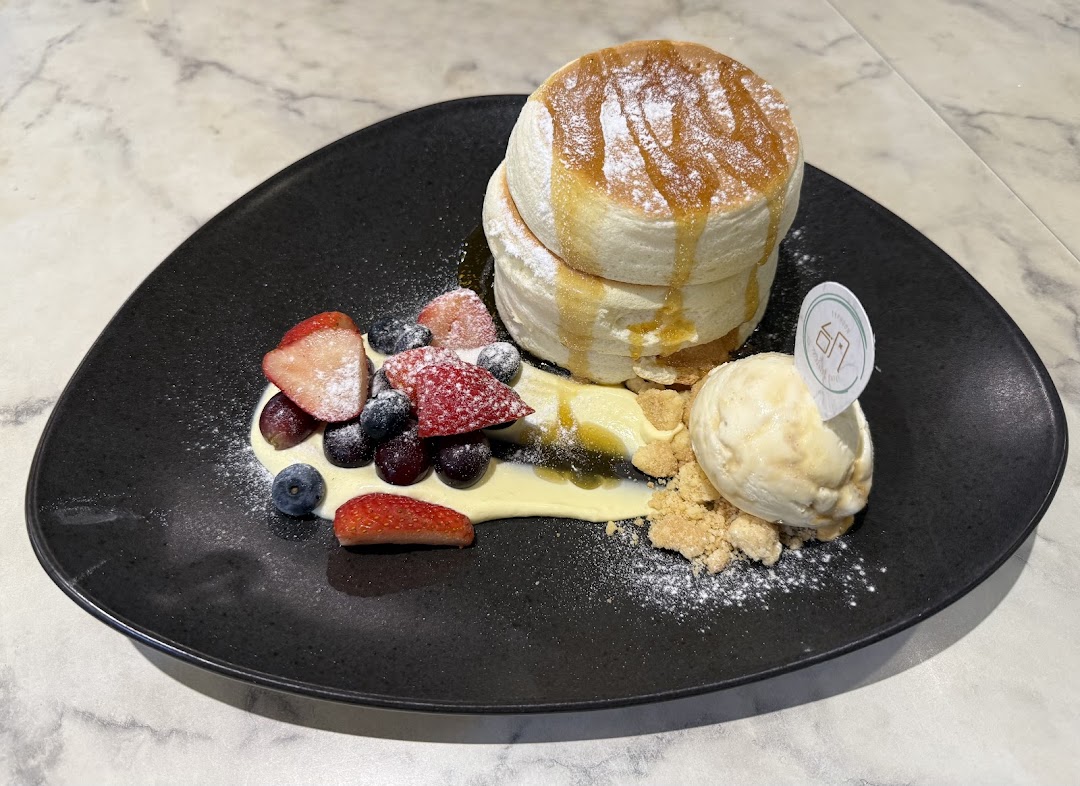A plate of fluffy soufflé pancakes with berries, vanilla ice cream, and syrup.