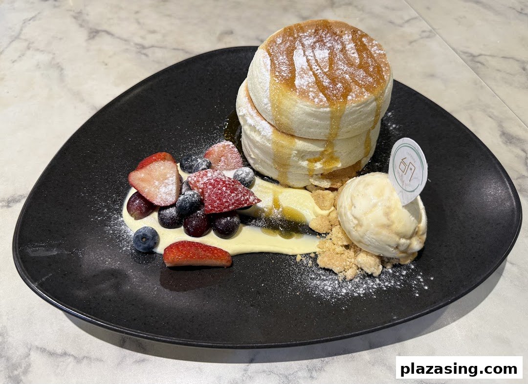 A plate of fluffy soufflé pancakes with berries, vanilla ice cream, and syrup.