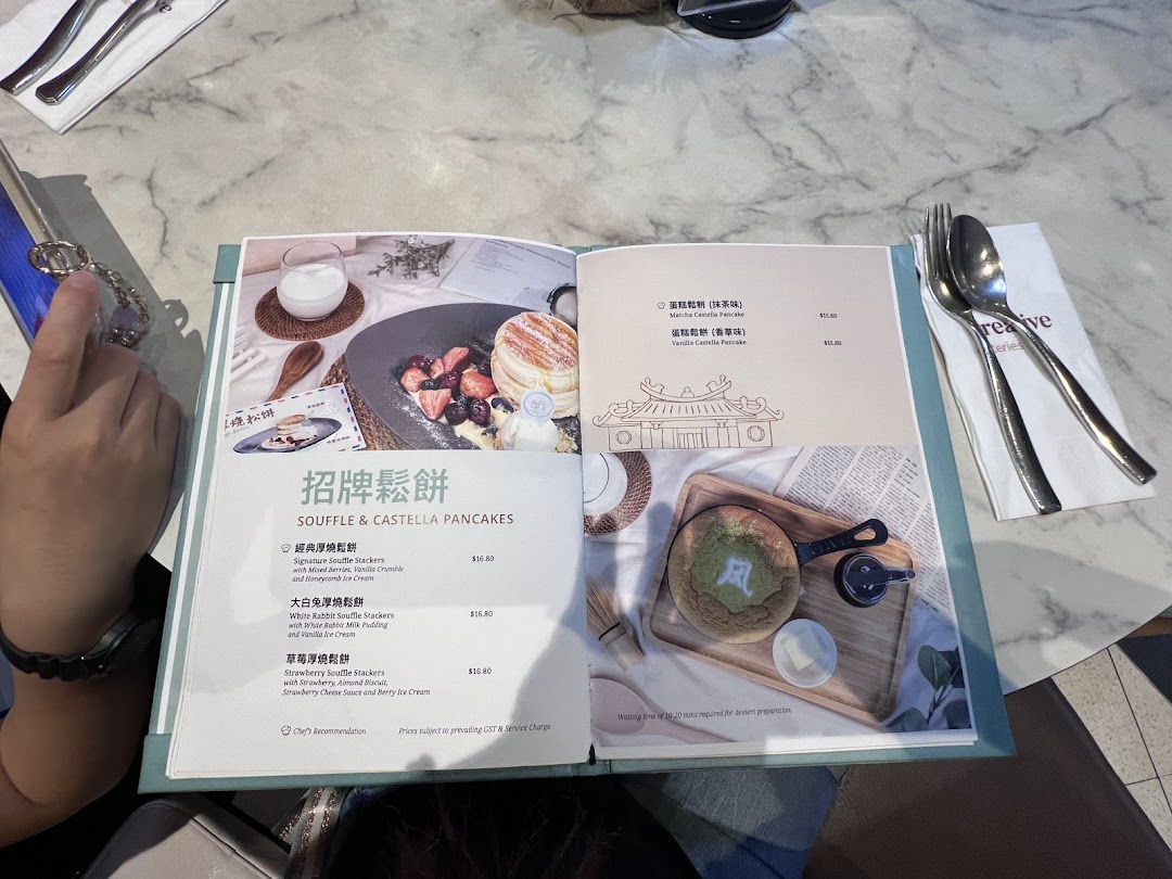 An open menu displaying various souffle and castella pancake options with prices at Typhoon Cafe.