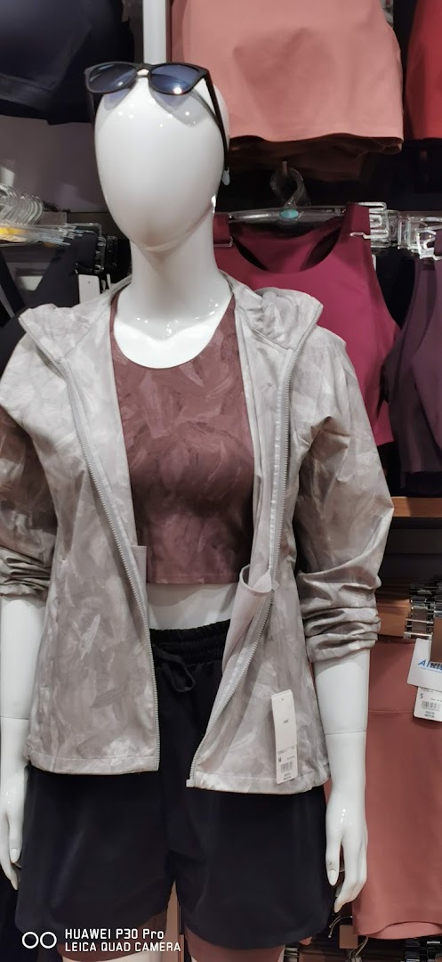 A mannequin displays a light grey jacket, a maroon sports bra, and black shorts in a retail store.