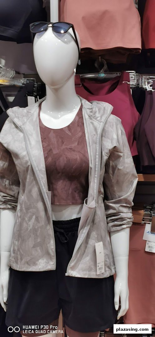 A mannequin displays a light grey jacket, a maroon sports bra, and black shorts in a retail store.