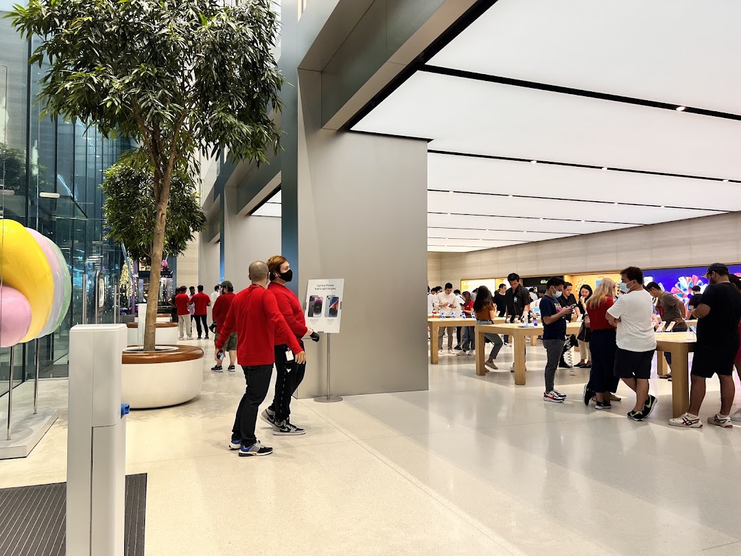 A bright, modern tech store interior with customers browsing products and staff in red shirts.