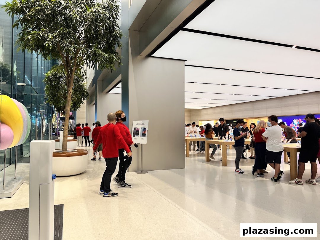 A bright, modern tech store interior with customers browsing products and staff in red shirts.