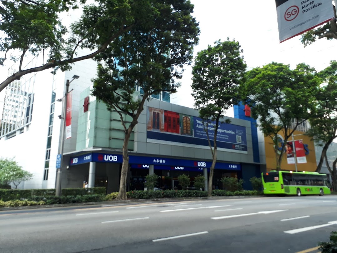 Exterior view of UOB Orchard Branch building with prominent signage, street, trees, and a green bus.
