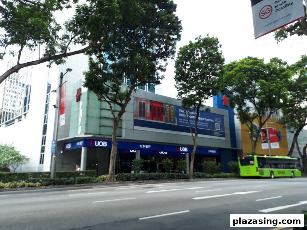 Exterior view of UOB Orchard Branch building with prominent signage, street, trees, and a green bus.