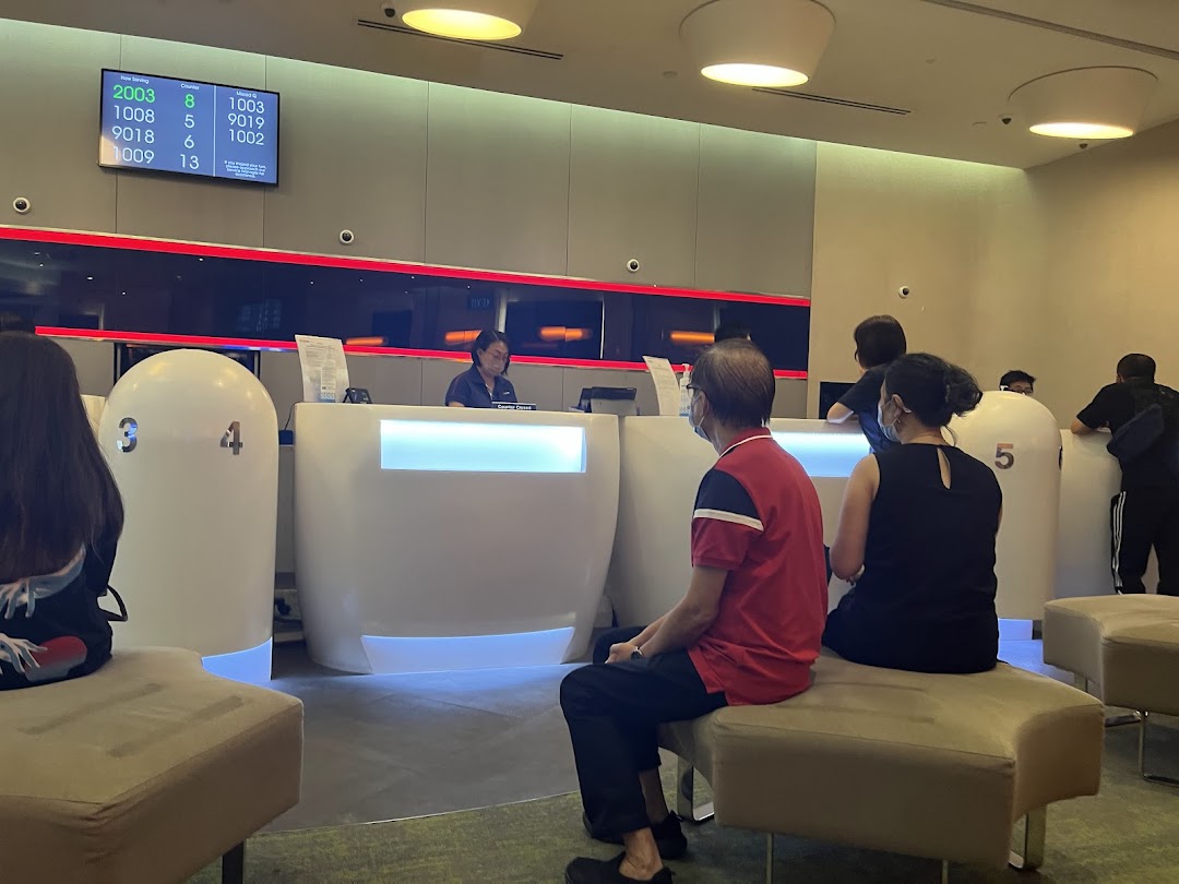 Customers waiting at service counters in a modern UOB bank branch, with a queue number display.