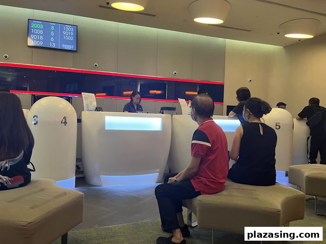 Customers waiting at service counters in a modern UOB bank branch, with a queue number display.