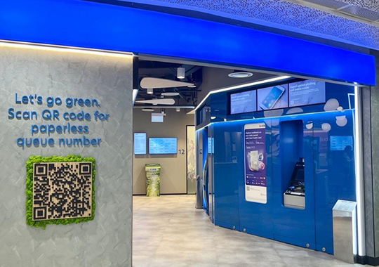 Entrance of UOB bank branch featuring a QR code for paperless queueing and digital service displays.