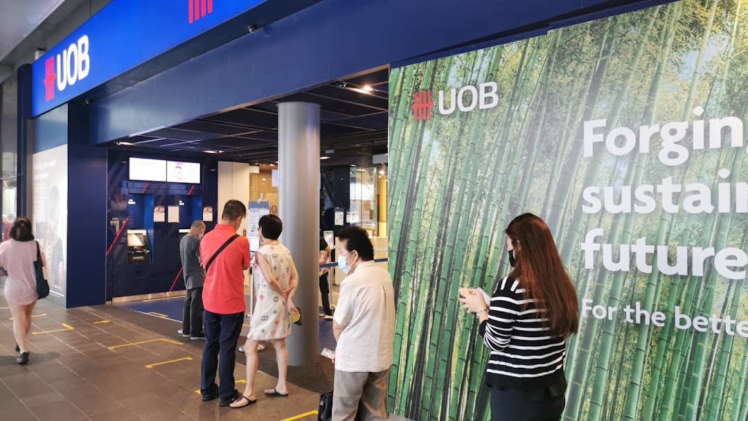 The UOB Orchard Branch entrance with customers queuing, showcasing the bank's prominent blue signage and green bamboo-themed branding.