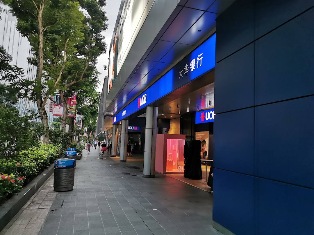 Exterior view of the UOB bank branch on a bustling street with pedestrians and lush greenery.