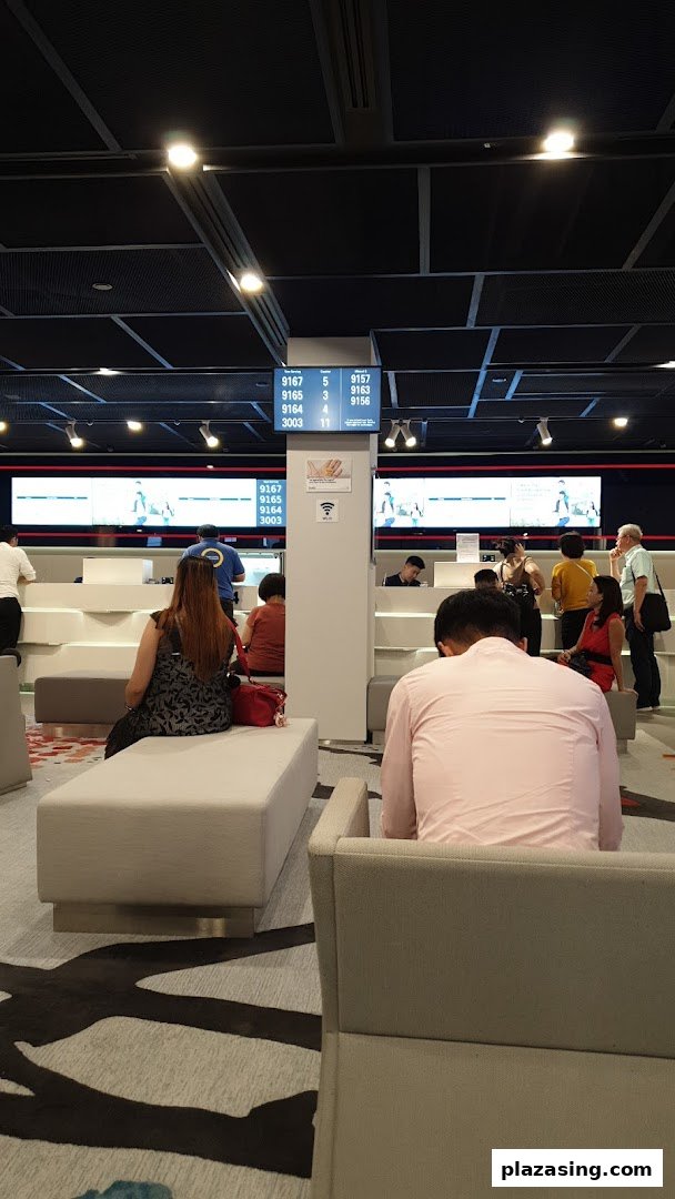 Customers waiting in a modern UOB bank branch with digital queue displays and service counters.