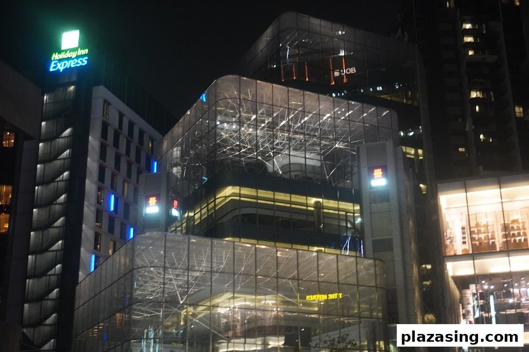 Night view of a modern building featuring illuminated signs for UOB and Holiday Inn Express.