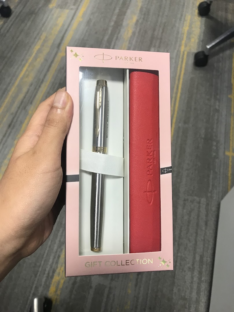 A hand holds a Parker pen and red case gift set in elegant pink packaging.