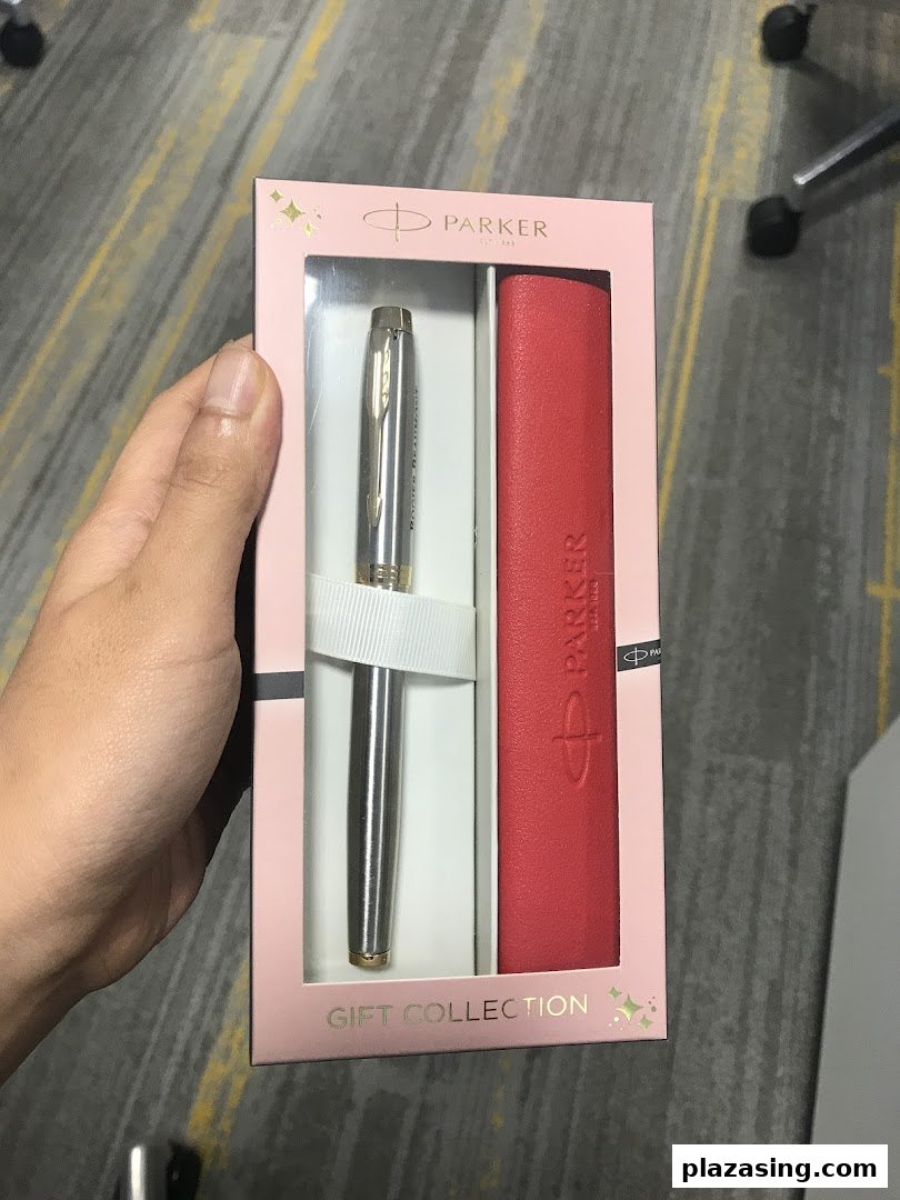 A hand holds a Parker pen and red case gift set in elegant pink packaging.
