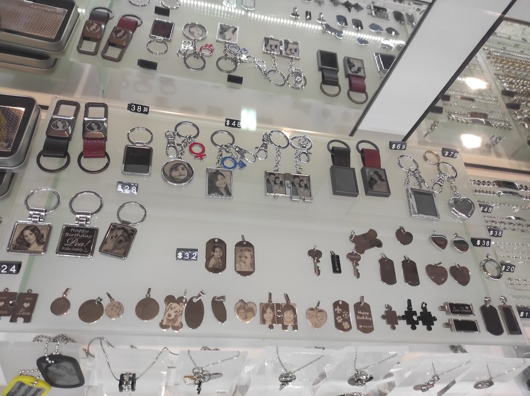 A display case showcasing various personalized keychains, pendants, and engraved metal accessories with photos and text.