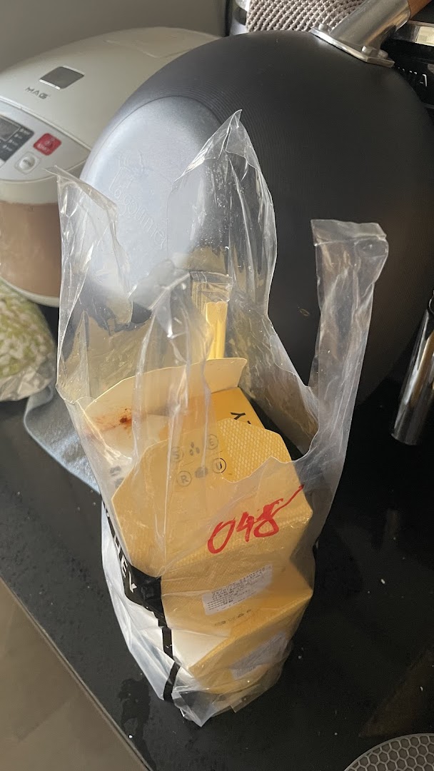 A clear plastic bag holds several yellow takeaway food containers from WOK HEY on a kitchen counter.