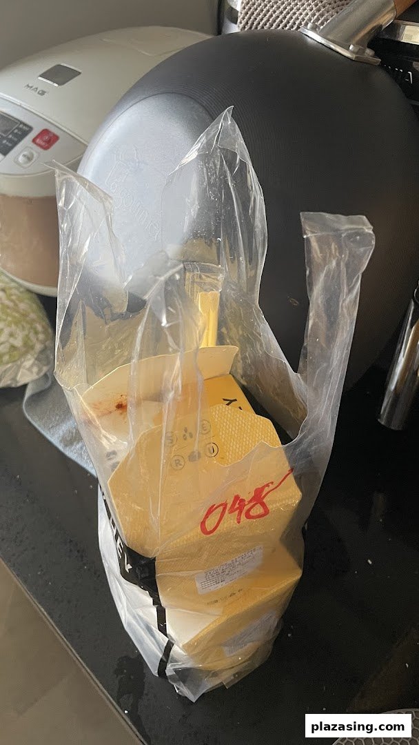 A clear plastic bag holds several yellow takeaway food containers from WOK HEY on a kitchen counter.