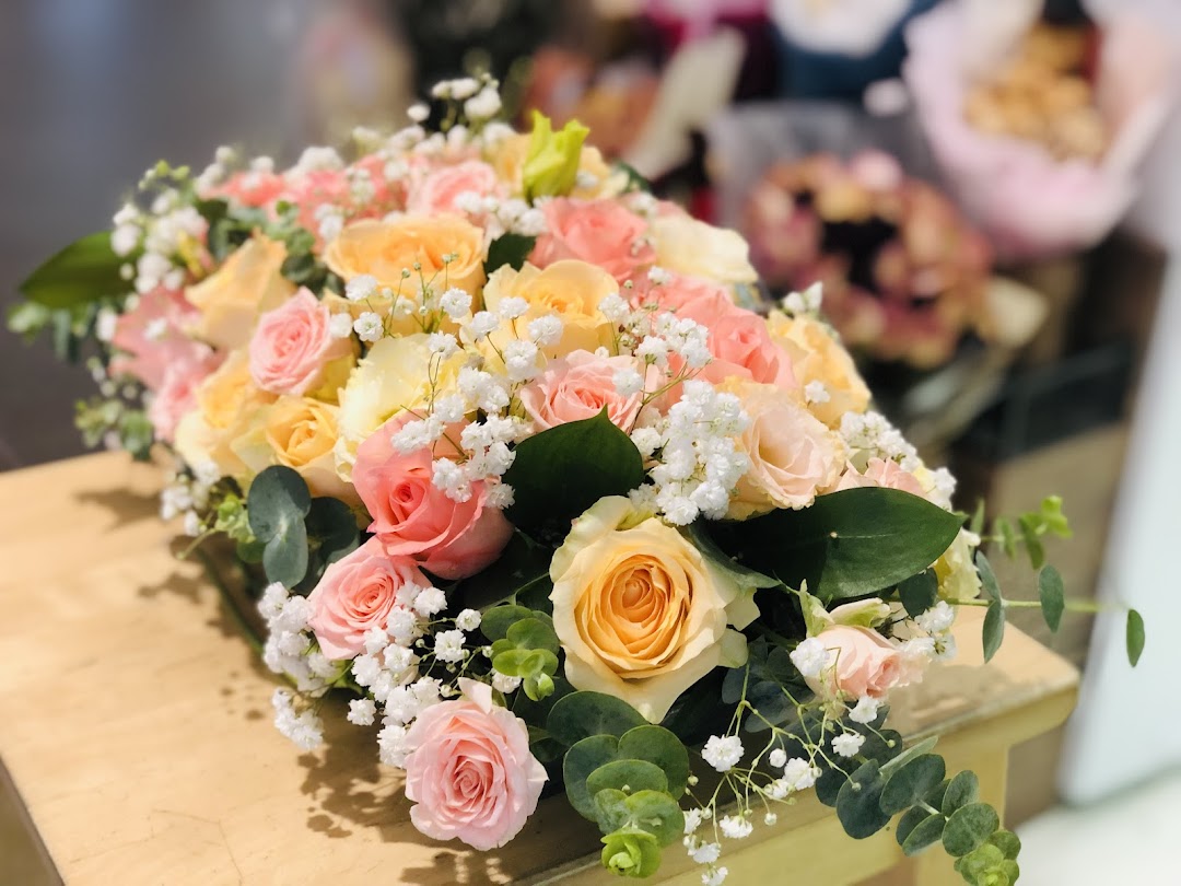 A vibrant bouquet of pink, peach, and yellow roses with baby's breath and eucalyptus on a wooden surface.