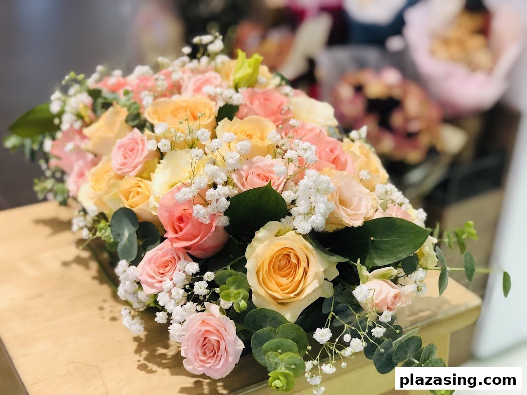 A vibrant bouquet of pink, peach, and yellow roses with baby's breath and eucalyptus on a wooden surface.