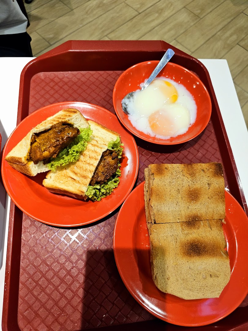 A tray with a sandwich, soft-boiled eggs, and toast, typical of a Ya Kun Kaya Toast meal.