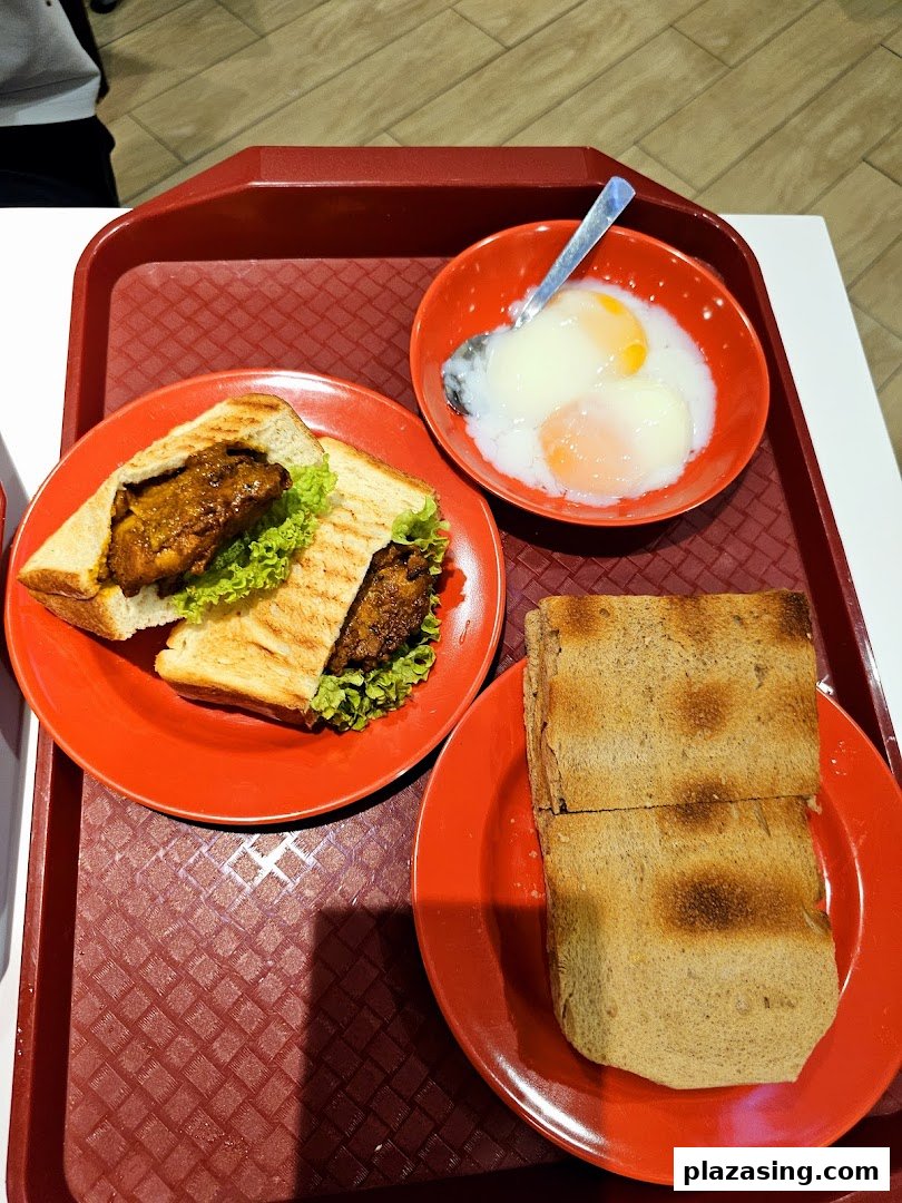 A tray with a sandwich, soft-boiled eggs, and toast, typical of a Ya Kun Kaya Toast meal.