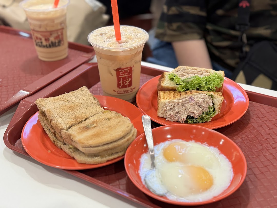A tray featuring traditional kaya toast, soft-boiled eggs, a tuna sandwich, and iced beverages from Ya Kun Kaya Toast.