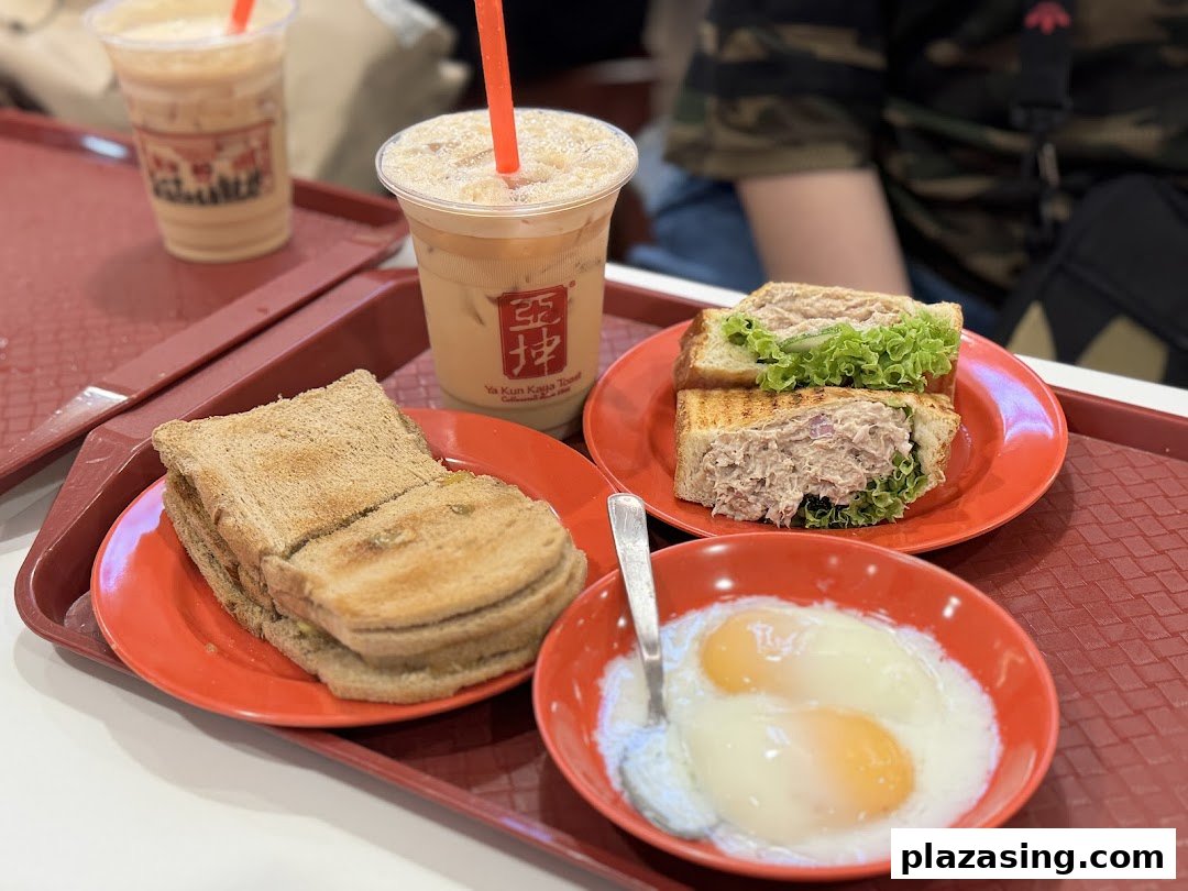 A tray featuring traditional kaya toast, soft-boiled eggs, a tuna sandwich, and iced beverages from Ya Kun Kaya Toast.