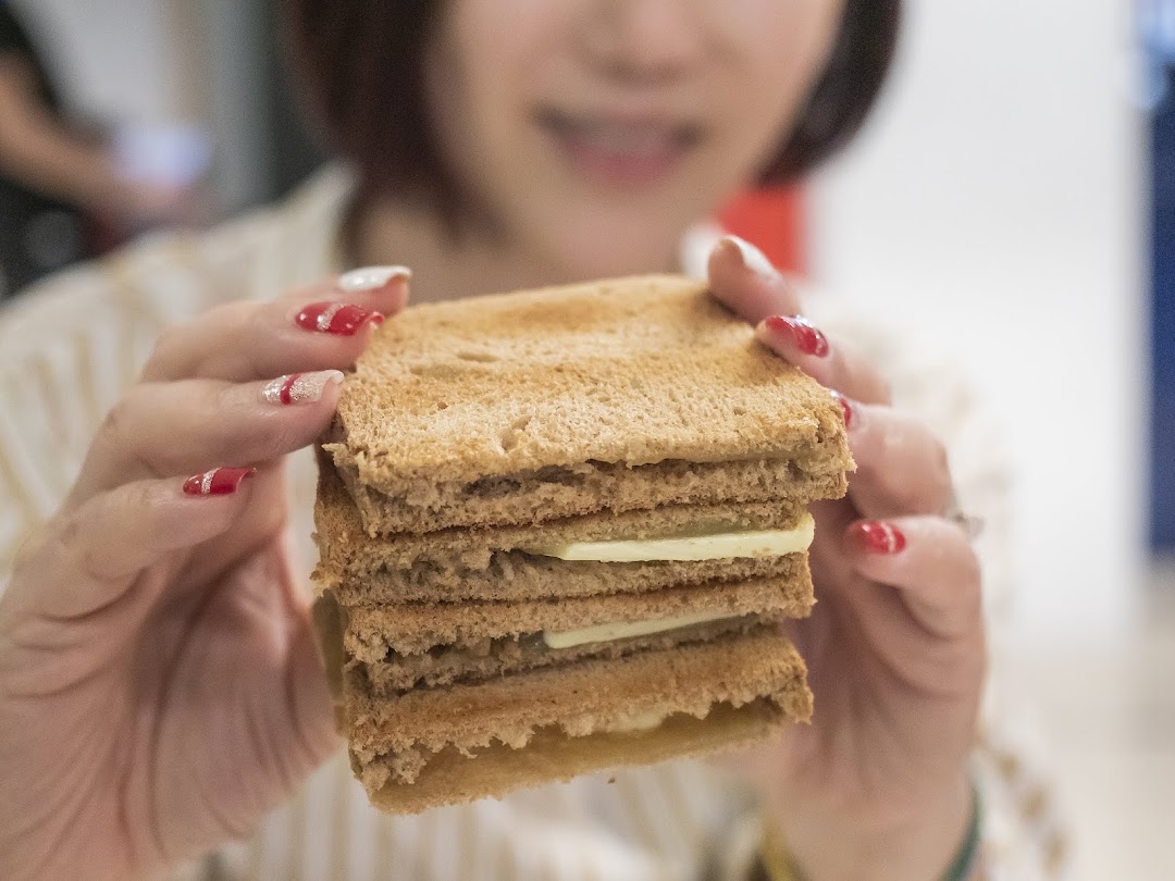 A person holds a stack of golden-brown kaya toast with butter slices, ready to enjoy.