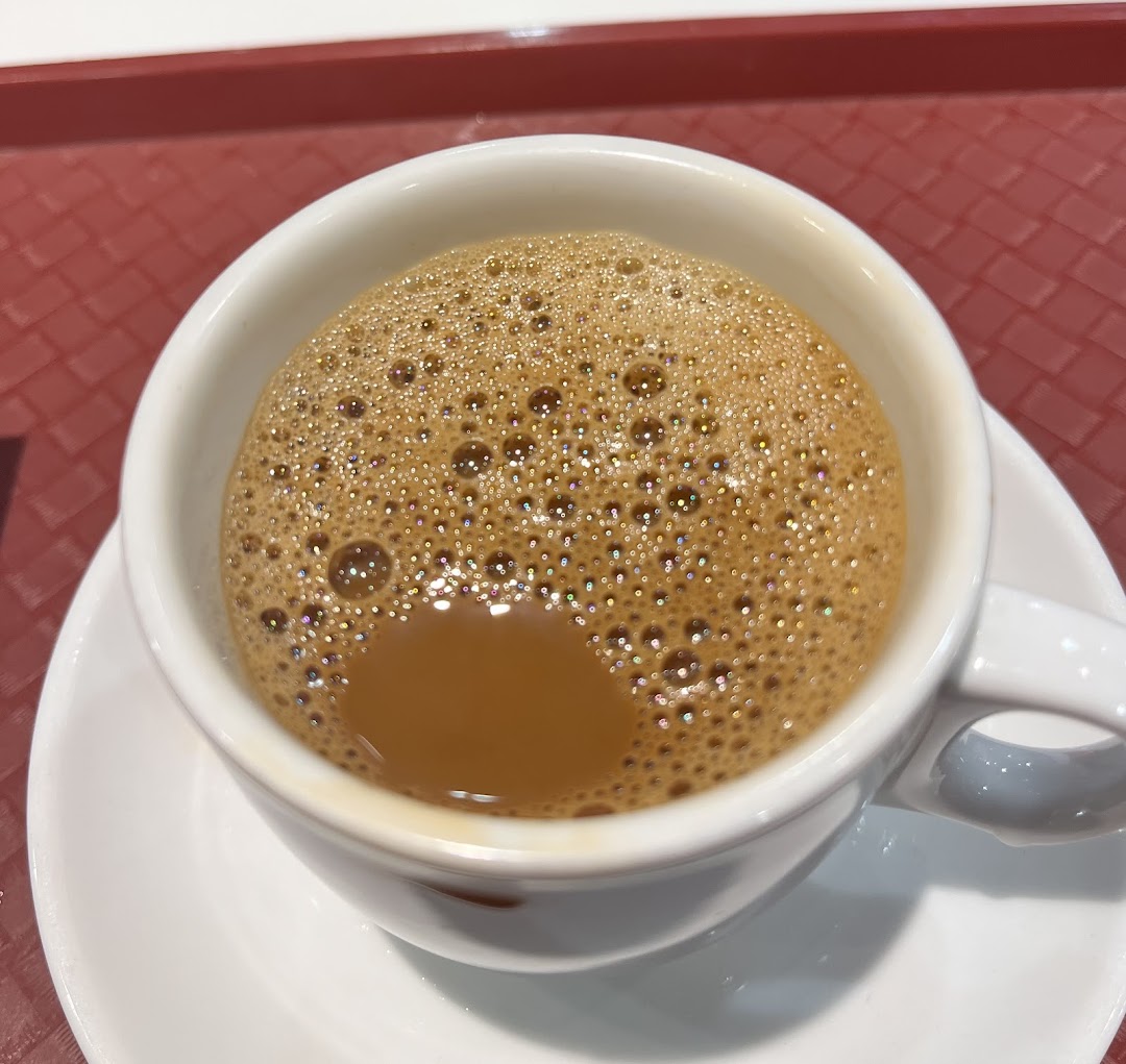 A close-up of a frothy cup of traditional coffee or tea from Ya Kun Kaya Toast, on a red tray.