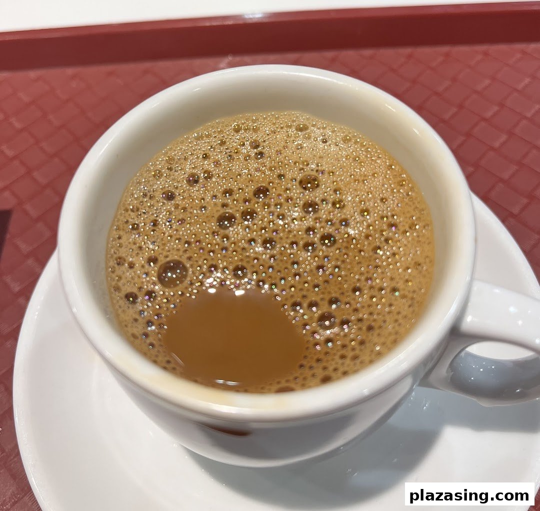A close-up of a frothy cup of traditional coffee or tea from Ya Kun Kaya Toast, on a red tray.