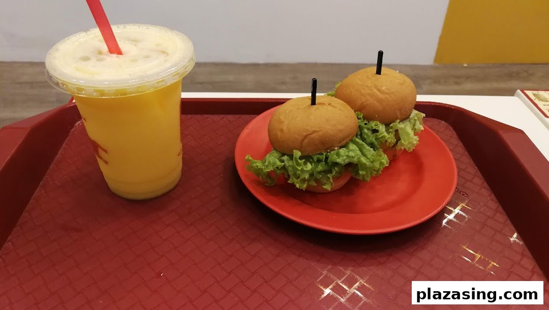 A vibrant yellow drink and two mini burgers with lettuce on a red tray.