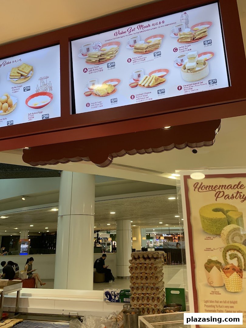 A brightly lit menu board at Ya Kun Kaya Toast displaying various value set meals and side dishes.