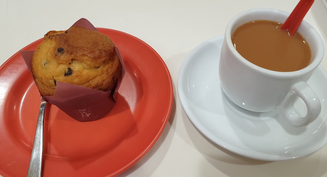 A delicious chocolate chip muffin on a red plate next to a cup of coffee or tea.