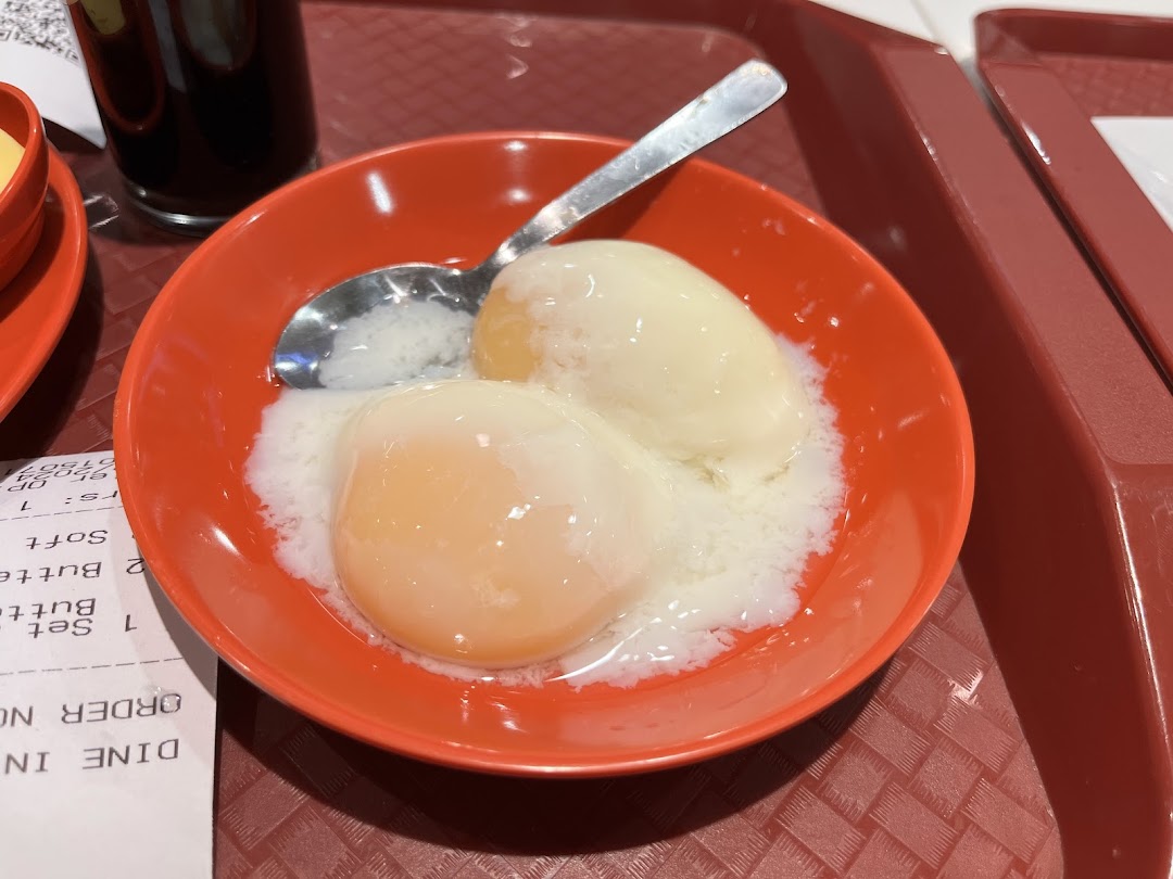 A close-up of traditional soft-boiled eggs in an orange bowl with a spoon, served on a red tray.