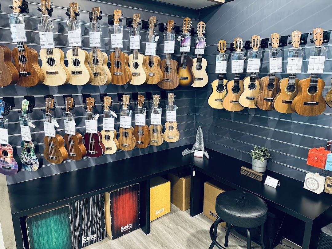 A vibrant display of ukuleles and guitars on a slat wall, showcasing various models and sizes in a music store.