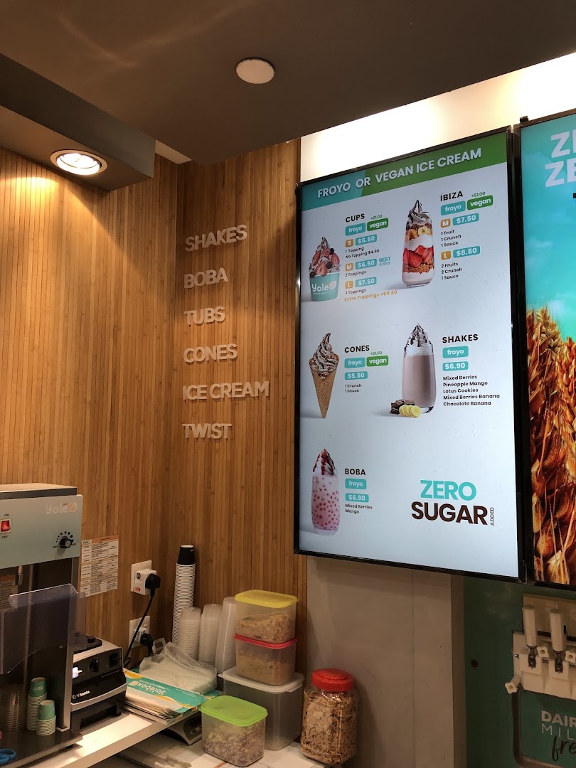 A digital menu board at Yolé, showcasing various frozen yogurt and vegan ice cream options.