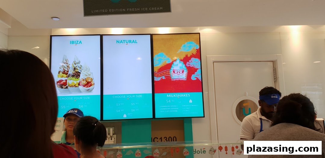 Digital menu boards at Yolé displaying frozen yogurt and milkshake options with prices and customers at the counter.