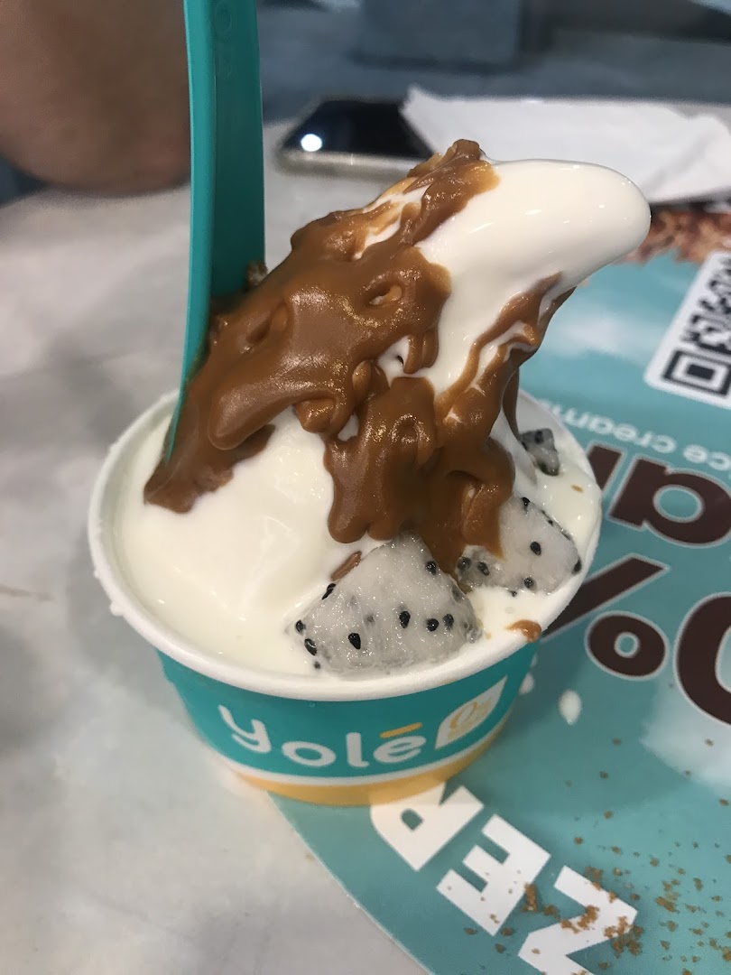 A close-up of a Yolé frozen yogurt cup topped with caramel sauce and fresh dragon fruit.