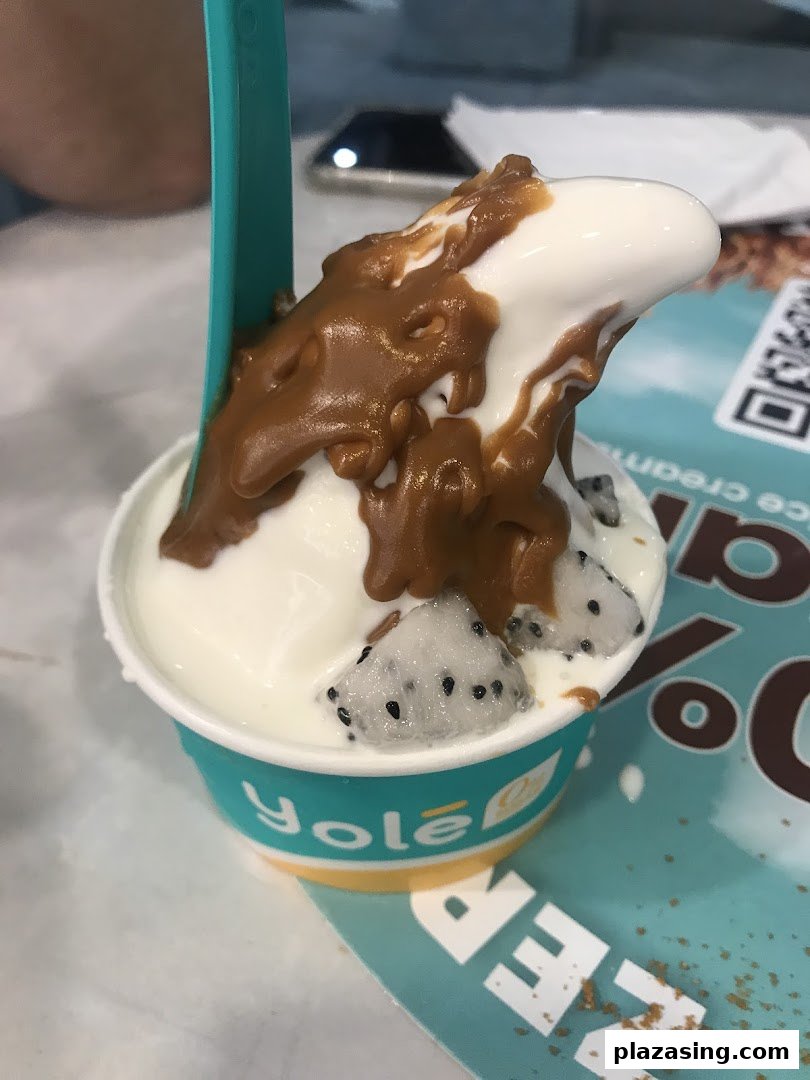 A close-up of a Yolé frozen yogurt cup topped with caramel sauce and fresh dragon fruit.